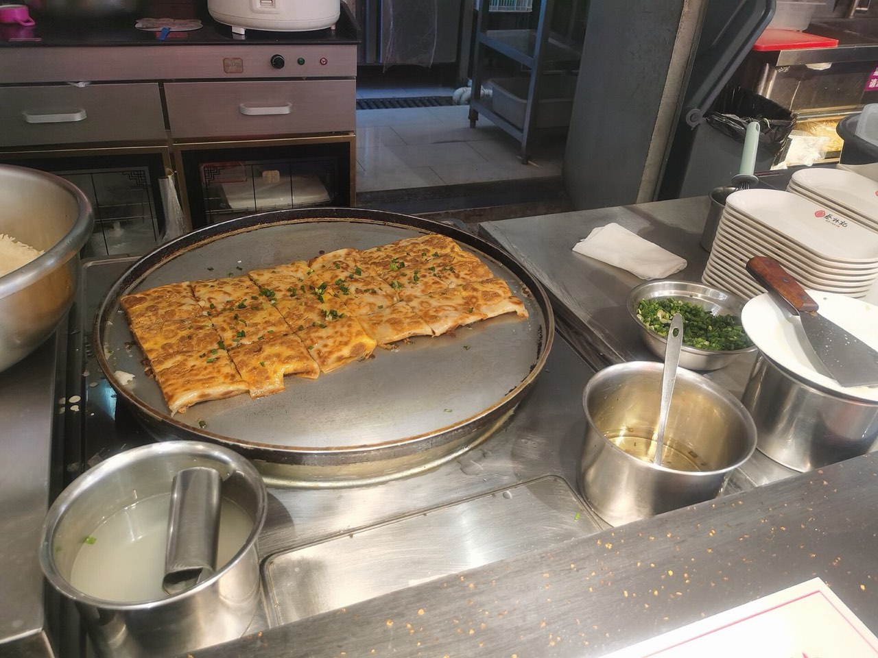 A large sheet of Wuhan doupi with a golden egg crust and sticky rice filling pan-fried on a round griddle at Cai Lin Ji