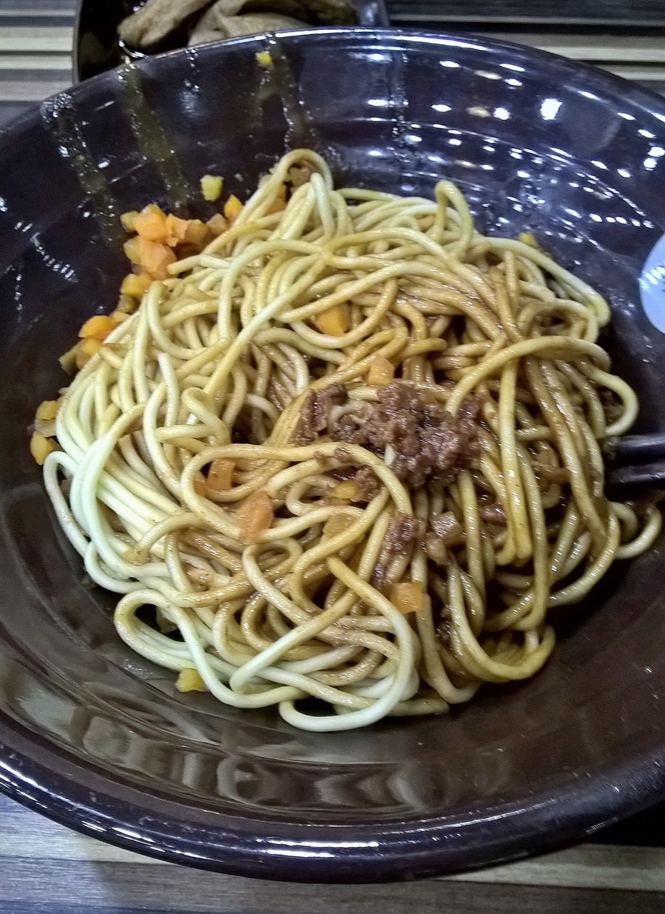 A bowl of Wuhan hot dry noodles (reganmian) coated in sesame paste, topped with pickled radish and minced pork