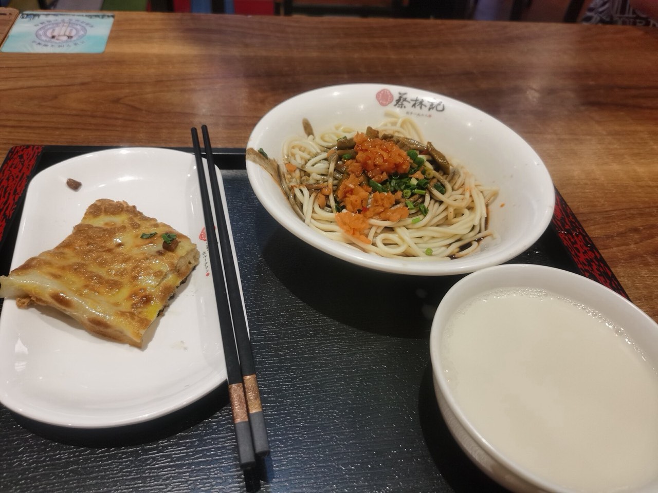 A classic Wuhan guozao breakfast set at Cai Lin Ji: hot dry noodles topped with pickled vegetables, a folded bean skin, and a bowl of soy milk